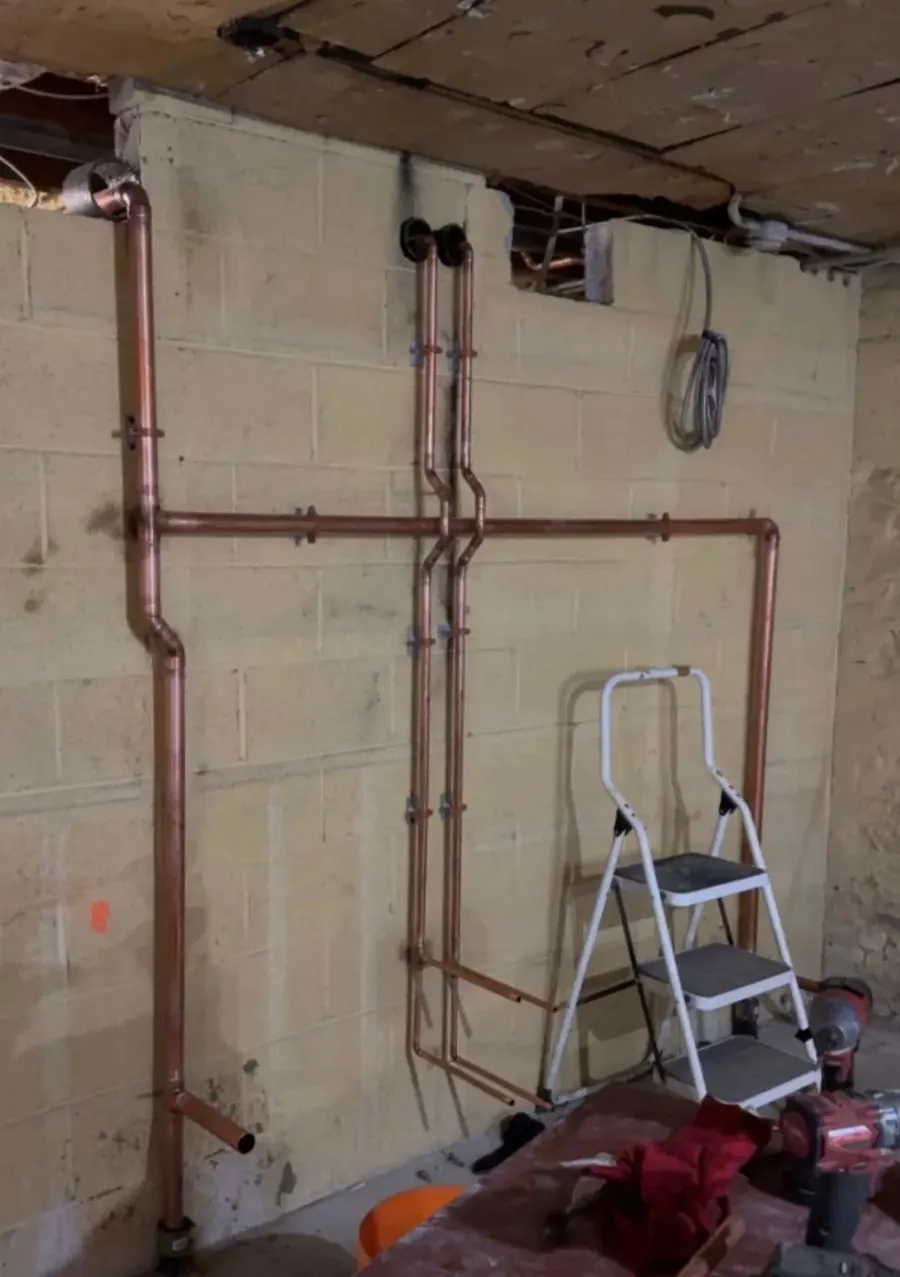 New copper supply lines running up and across an unfinished concrete block basement wall.