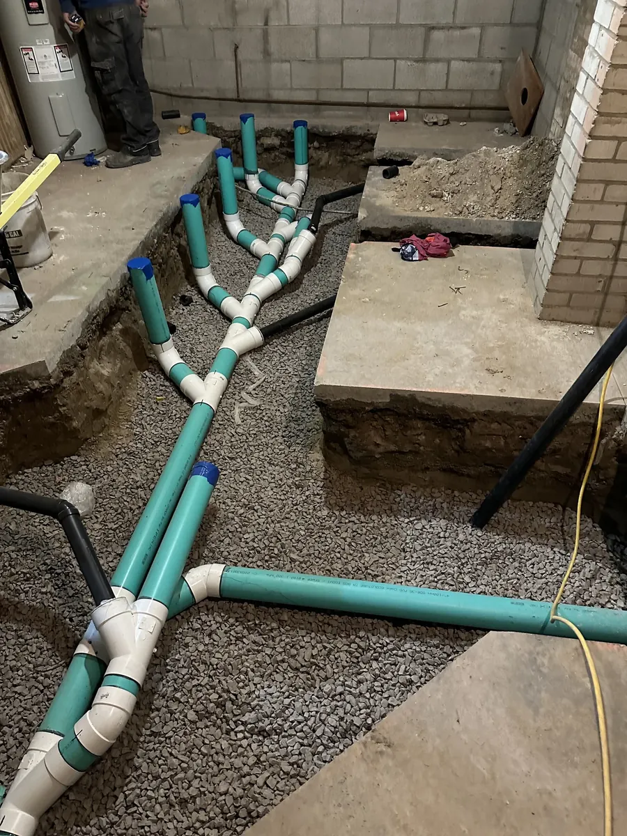 Green drain pipes and white fittings laid in gravel in a dug-out floor before the concrete is poured.
